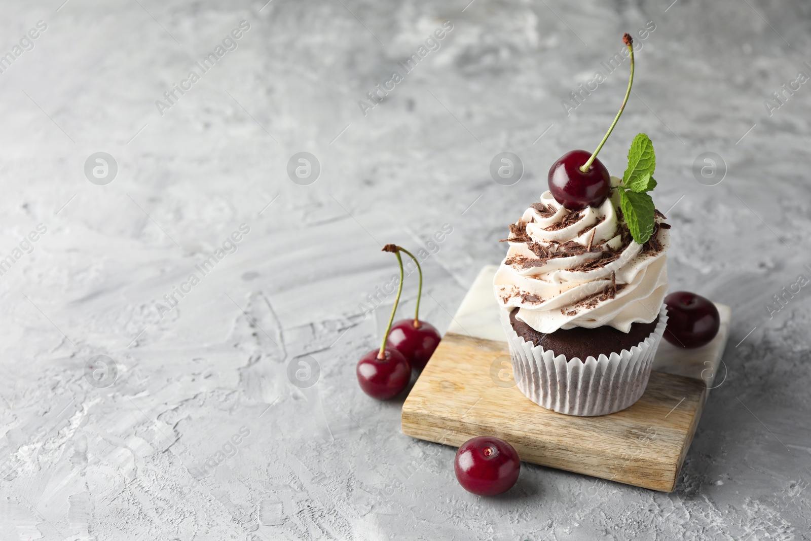 Photo of Delicious cupcake with cream and cherries on grey textured table, space for text