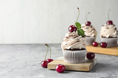 Photo of Delicious cupcake with cream and cherries on grey textured table, space for text