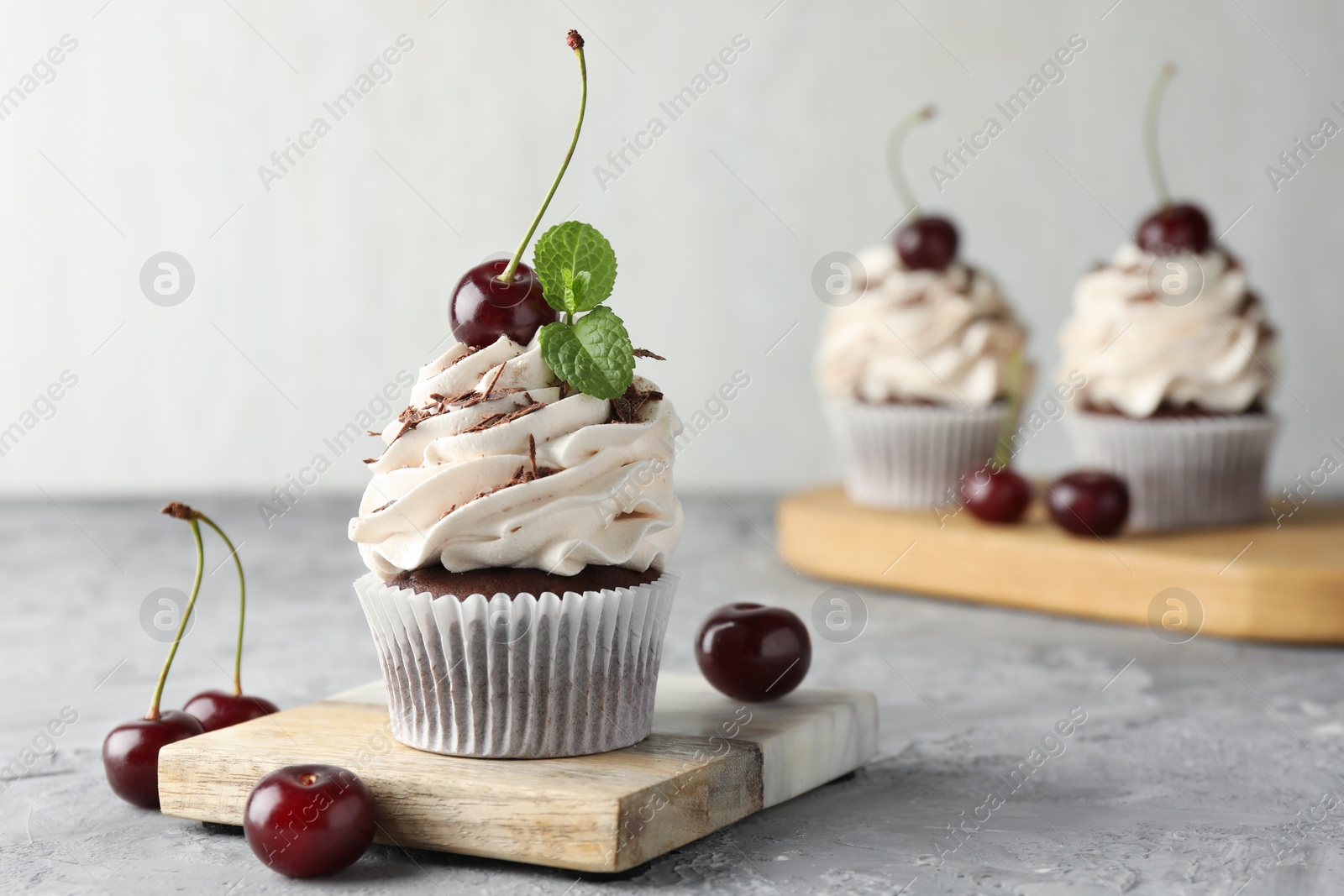 Photo of Delicious cupcake with cream and cherries on grey textured table