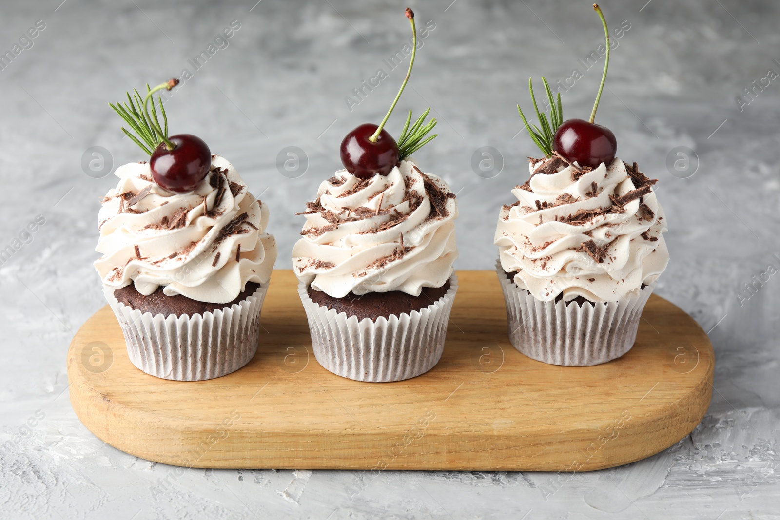 Photo of Delicious cupcakes with cream and cherries on grey textured table