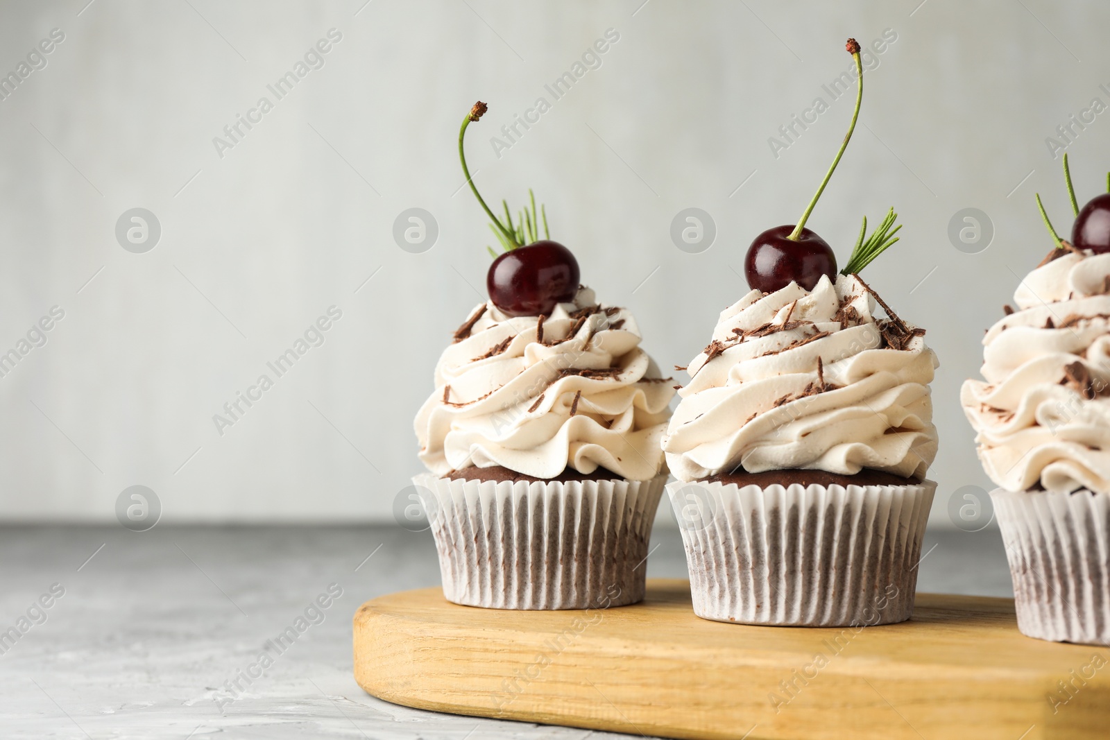 Photo of Delicious cupcakes with cream and cherries on grey textured table, closeup. Space for text