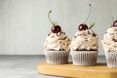 Photo of Delicious cupcakes with cream and cherries on grey textured table, closeup. Space for text