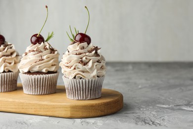 Photo of Delicious cupcakes with cream and cherries on grey textured table, space for text