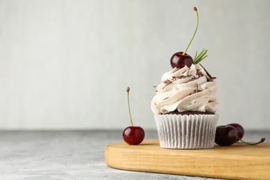 Delicious cupcake with cream and cherries on grey textured table. Space for text