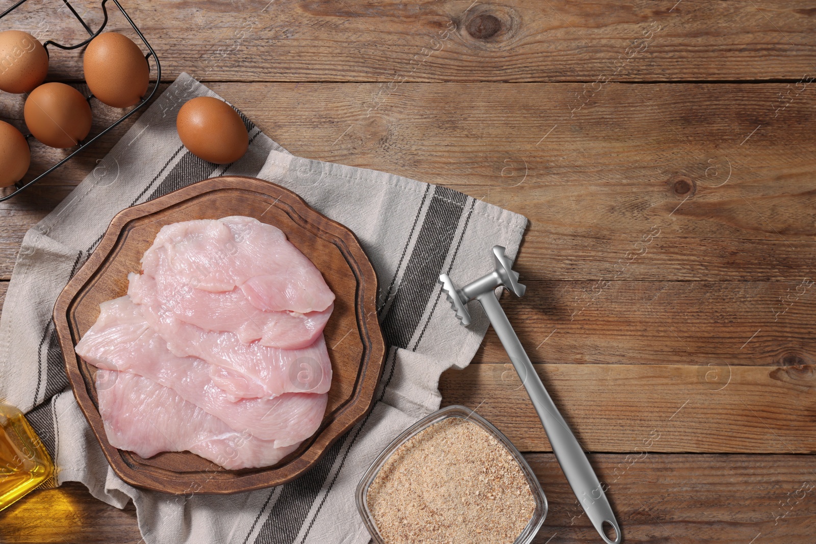 Photo of Making schnitzel. Raw meat, bread crumbs, eggs and tenderizer on wooden table, flat lay. Space for text