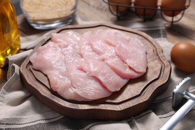 Making schnitzel. Board with raw meat and tenderizer on table, closeup