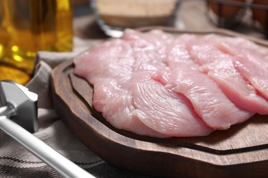 Making schnitzel. Board with raw meat and tenderizer on table, closeup