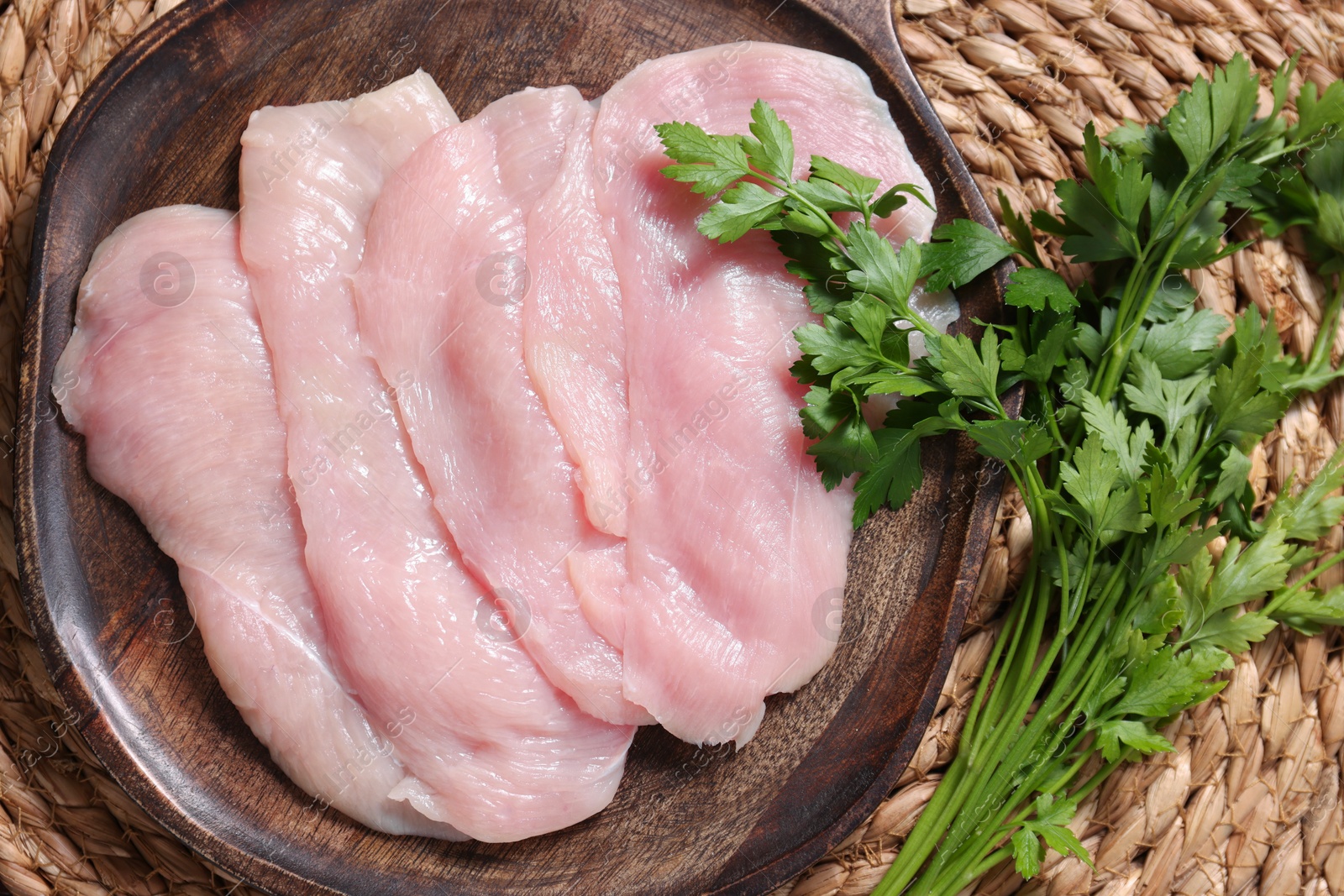 Photo of Making schnitzel. Board with raw meat and parsley on wicker mat, top view