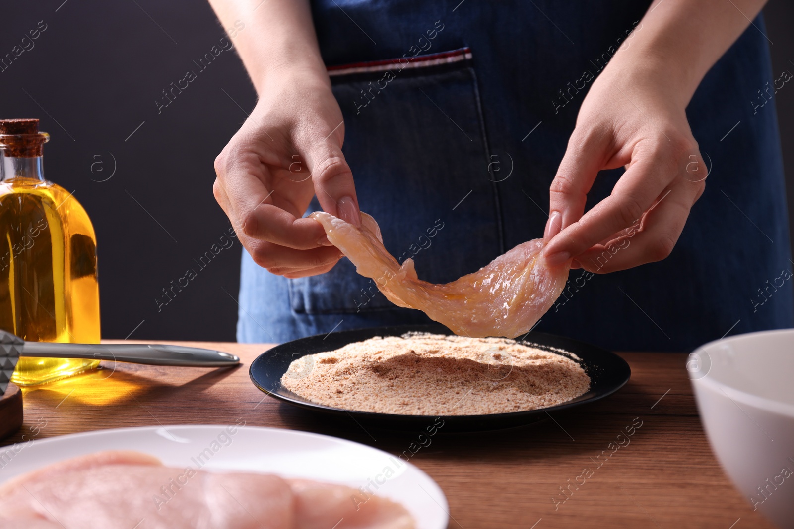 Photo of Making schnitzel. Woman coating slice of meat with bread crumbs at wooden table, closeup