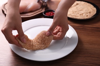 Photo of Making schnitzel. Woman coating slice of meat with bread crumbs at wooden table, closeup