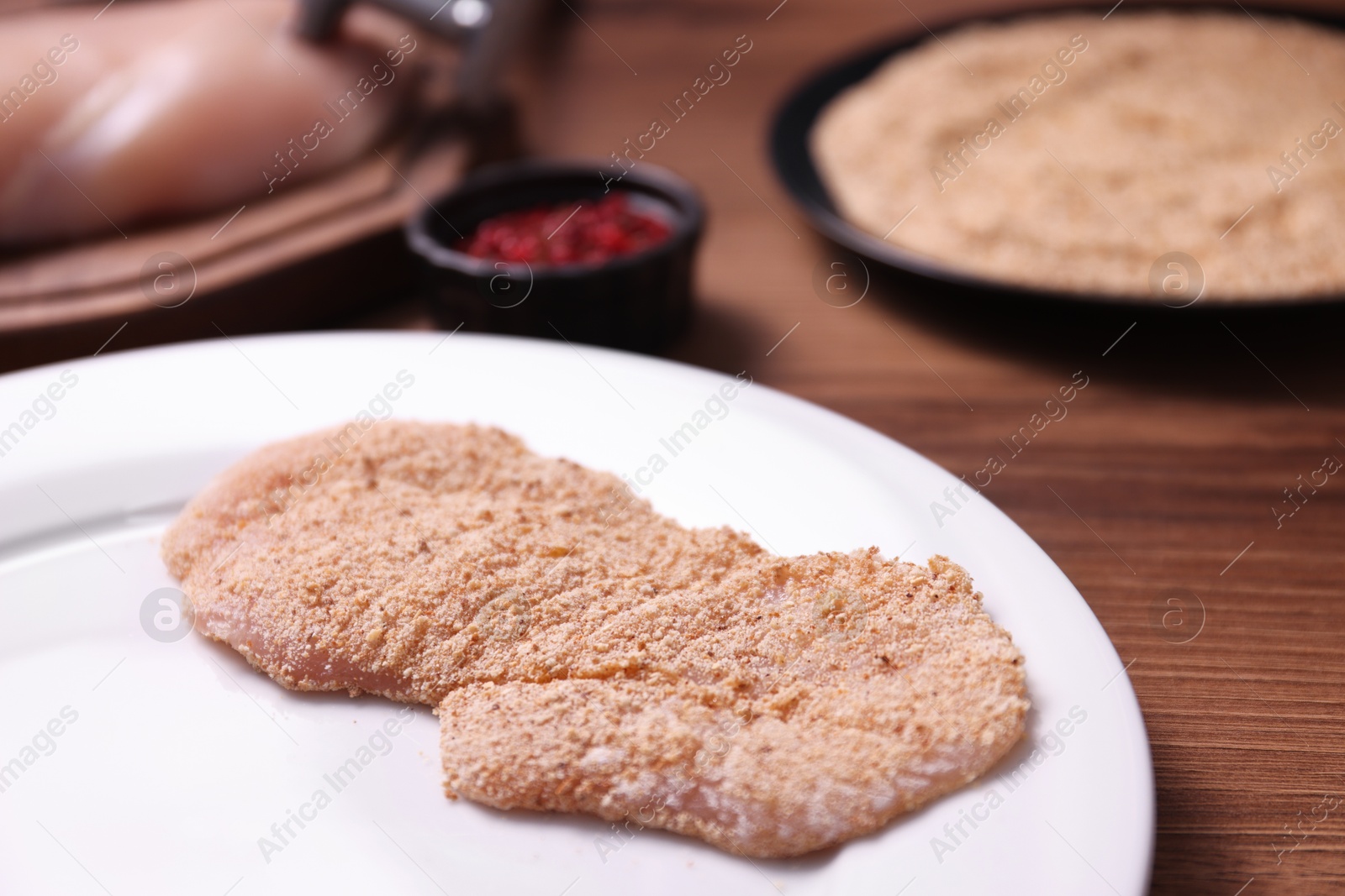 Photo of Making schnitzel. Plate with raw slice of meat in bread crumbs on wooden table, closeup