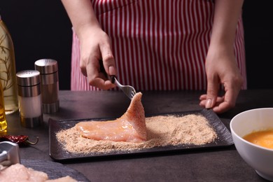 Making schnitzel. Woman coating slice of meat with bread crumbs at dark table, closeup