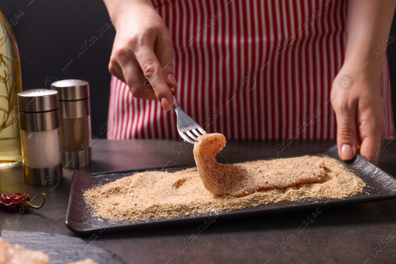 Photo of Making schnitzel. Woman coating slice of meat with bread crumbs at dark table, closeup