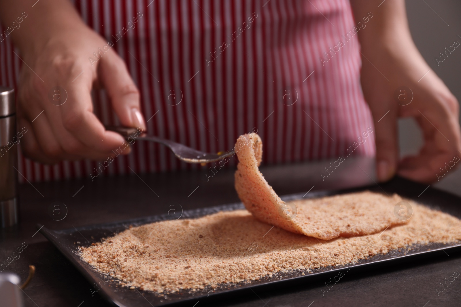 Photo of Making schnitzel. Woman coating slice of meat with bread crumbs at dark table, closeup