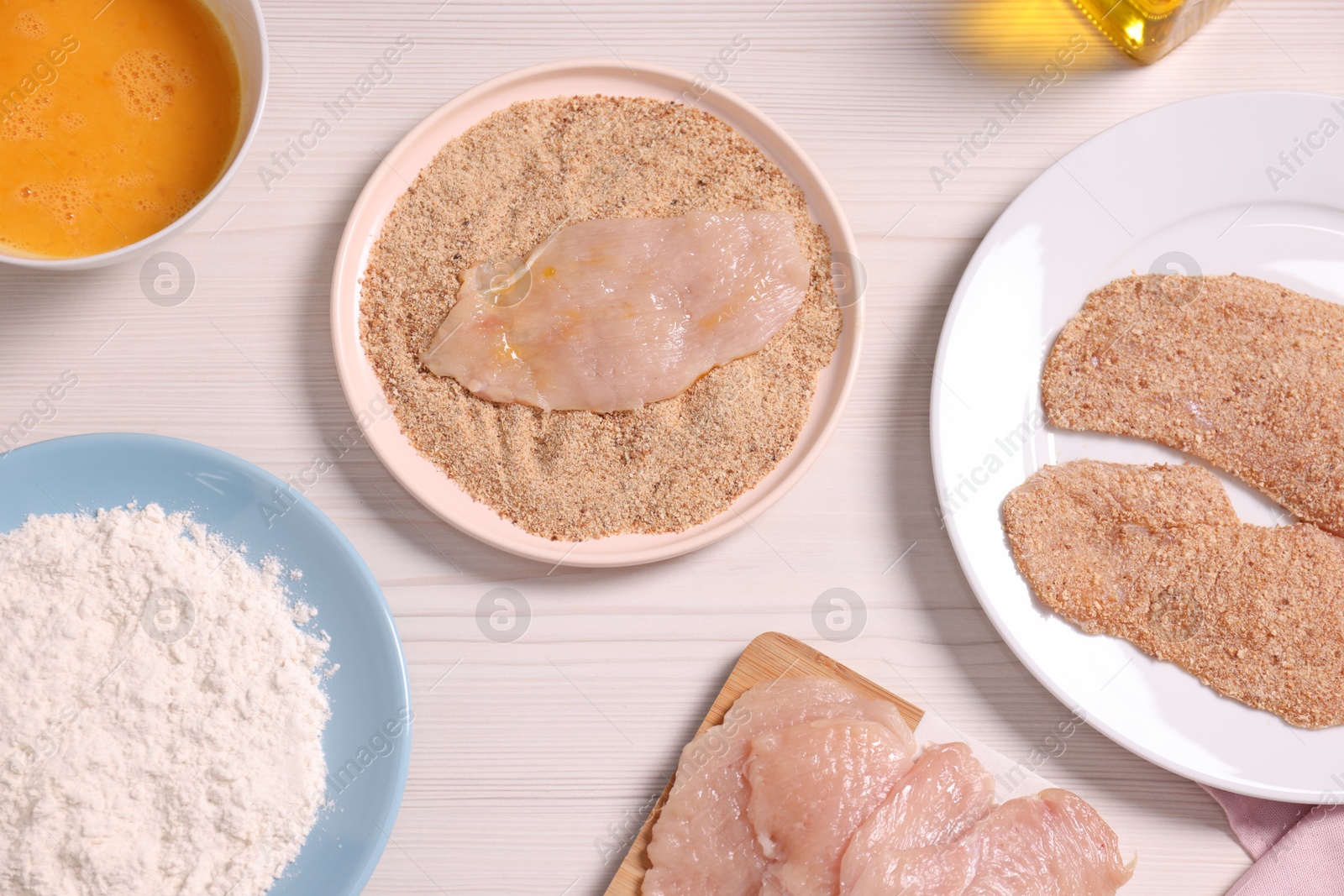 Photo of Making schnitzel. Slices of meat with bread crumbs and ingredients on white wooden table, flat lay