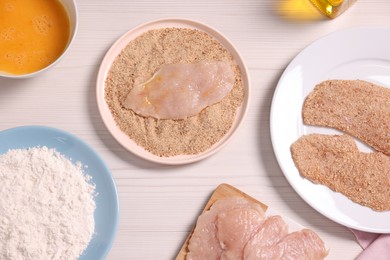 Making schnitzel. Slices of meat with bread crumbs and ingredients on white wooden table, flat lay