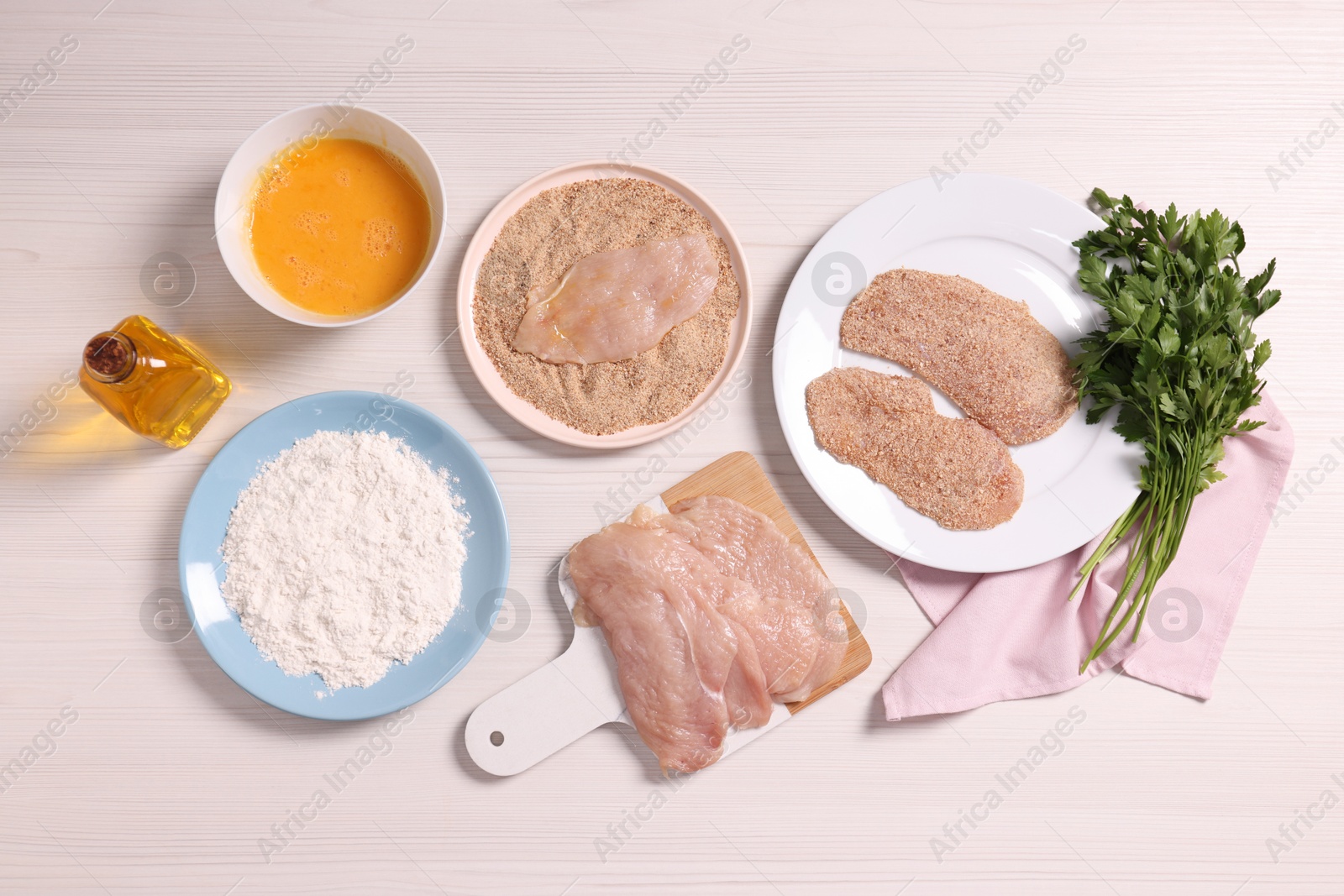 Photo of Making schnitzel. Slices of meat with bread crumbs and ingredients on white wooden table, flat lay