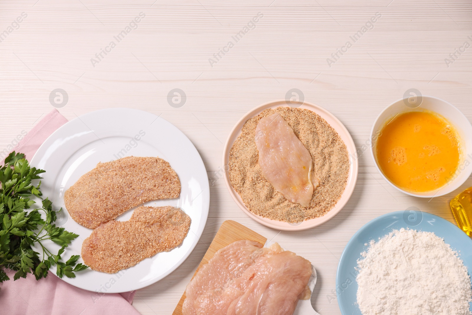 Photo of Making schnitzel. Slices of meat with bread crumbs and ingredients on white wooden table, flat lay