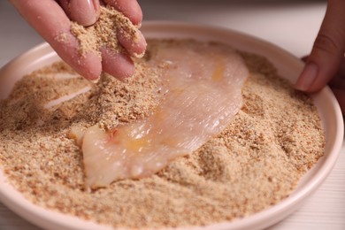 Photo of Making schnitzel. Woman coating slice of meat with bread crumbs at white wooden table, closeup