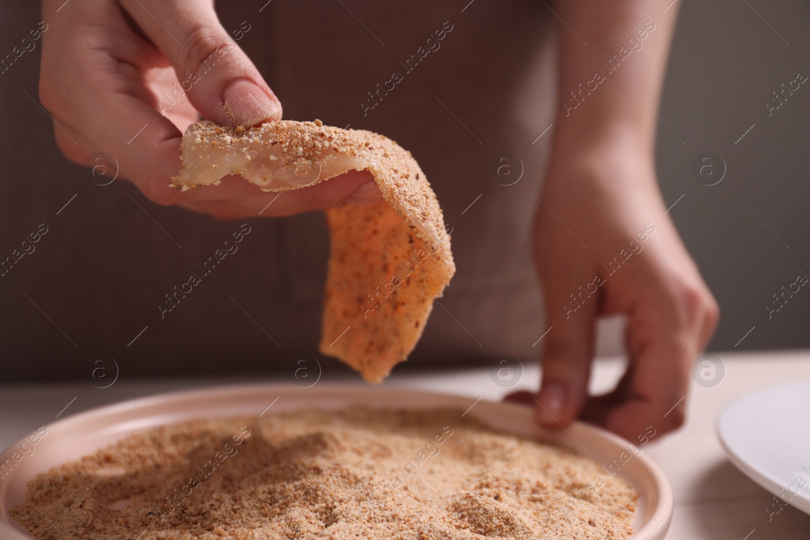 Photo of Making schnitzel. Woman coating slice of meat with bread crumbs at white table, closeup