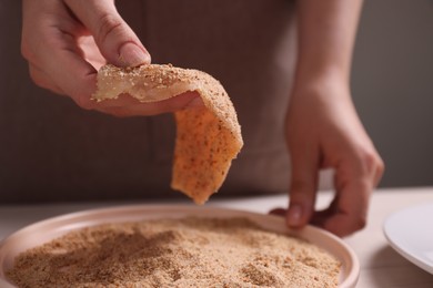 Making schnitzel. Woman coating slice of meat with bread crumbs at white table, closeup