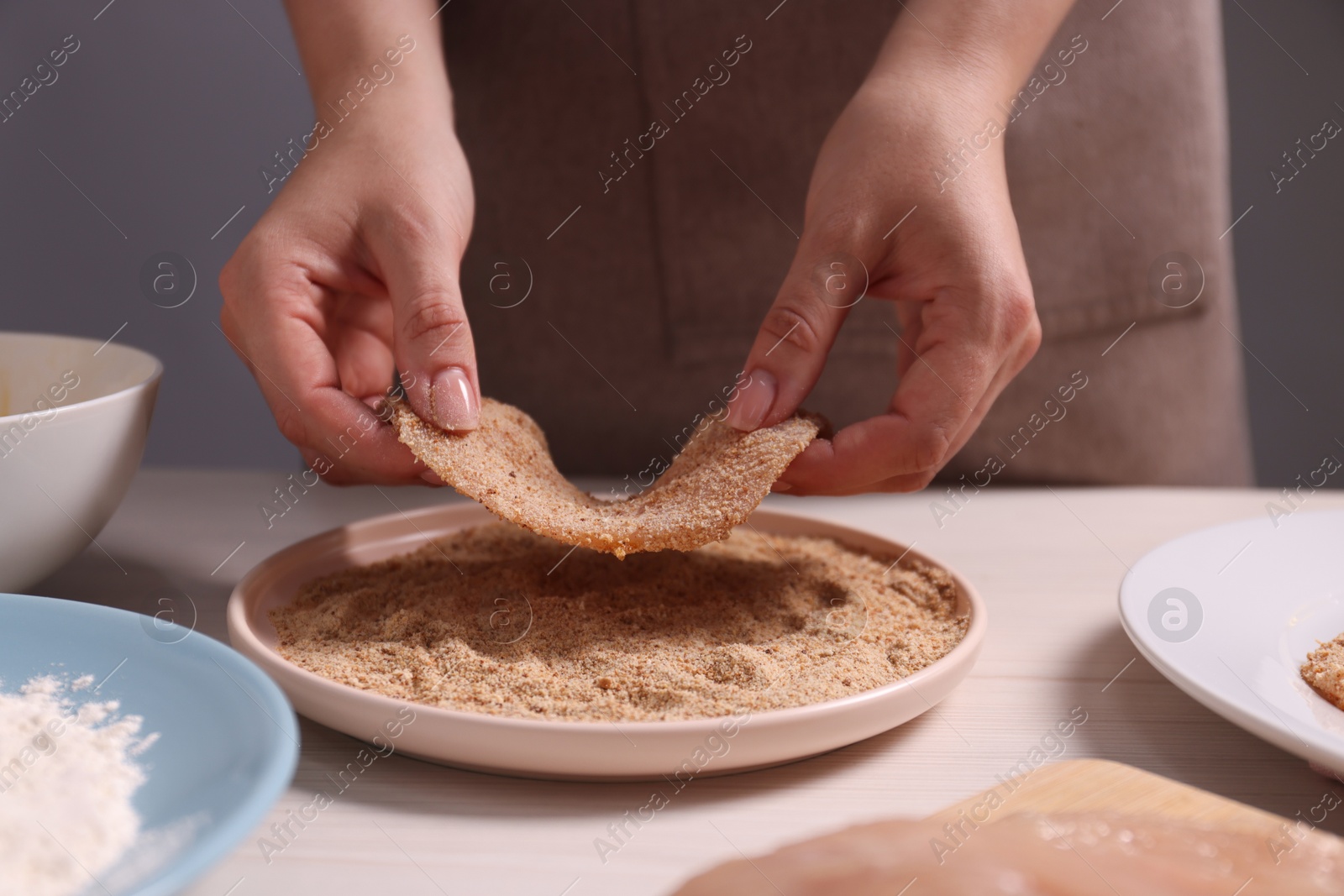 Photo of Making schnitzel. Woman coating slice of meat with bread crumbs at white wooden table, closeup