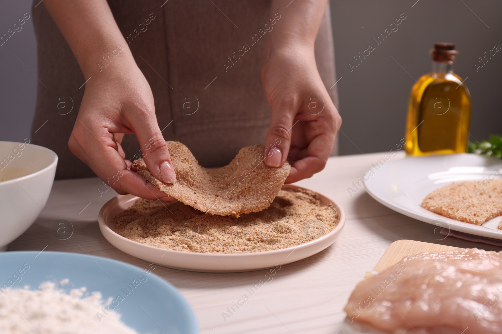 Photo of Making schnitzel. Woman coating slice of meat with bread crumbs at white wooden table, closeup