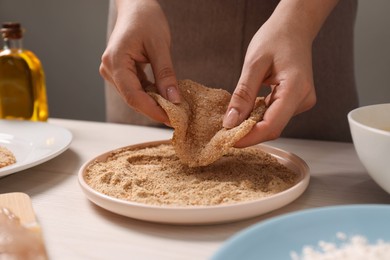 Making schnitzel. Woman coating slice of meat with bread crumbs at white wooden table, closeup