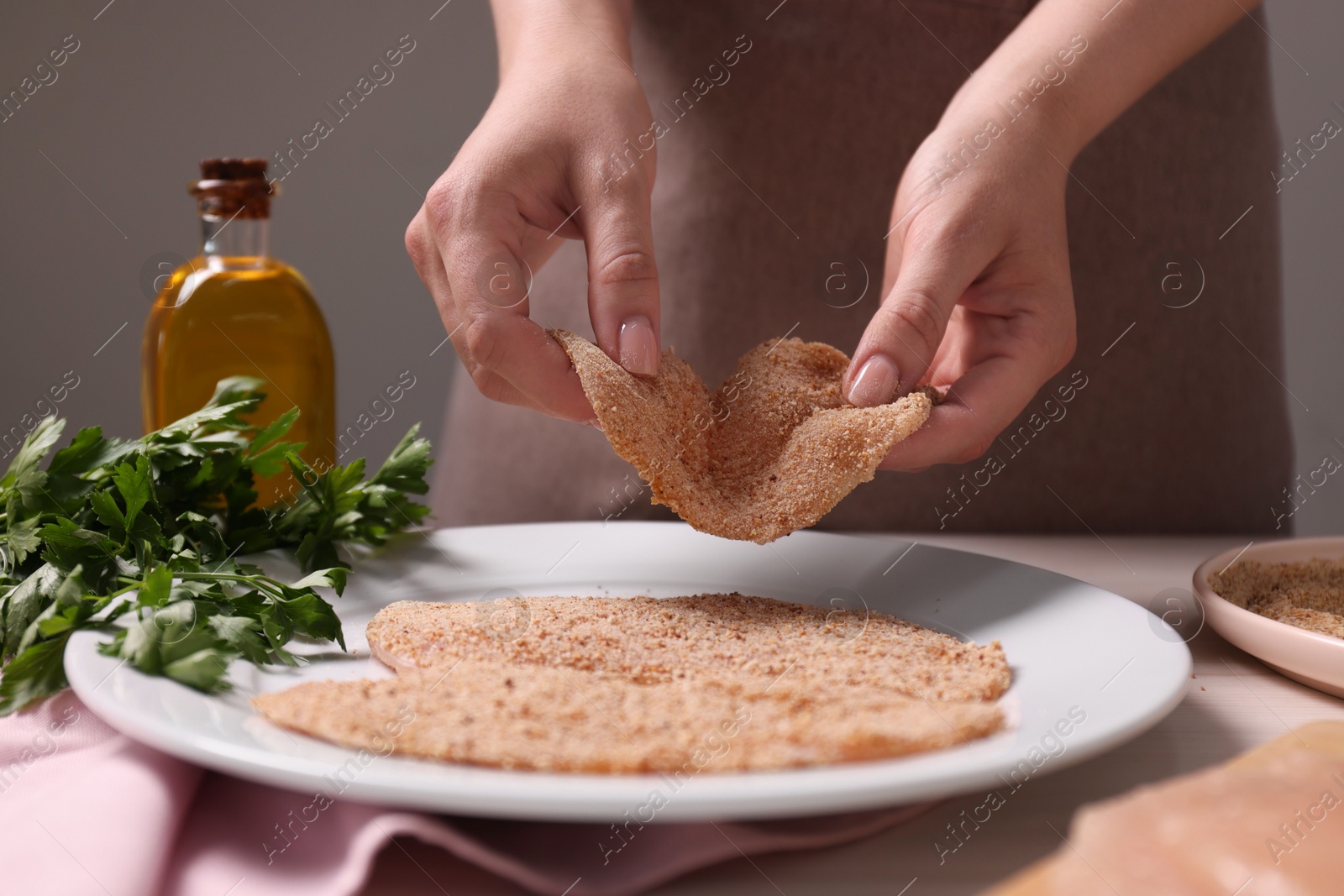 Photo of Making schnitzel. Woman putting slice of meat with bread crumbs onto plate at table, closeup