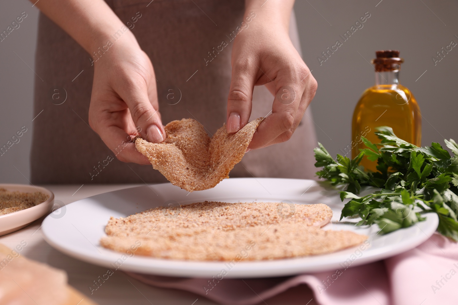 Photo of Making schnitzel. Woman putting slice of meat with bread crumbs onto plate at table, closeup