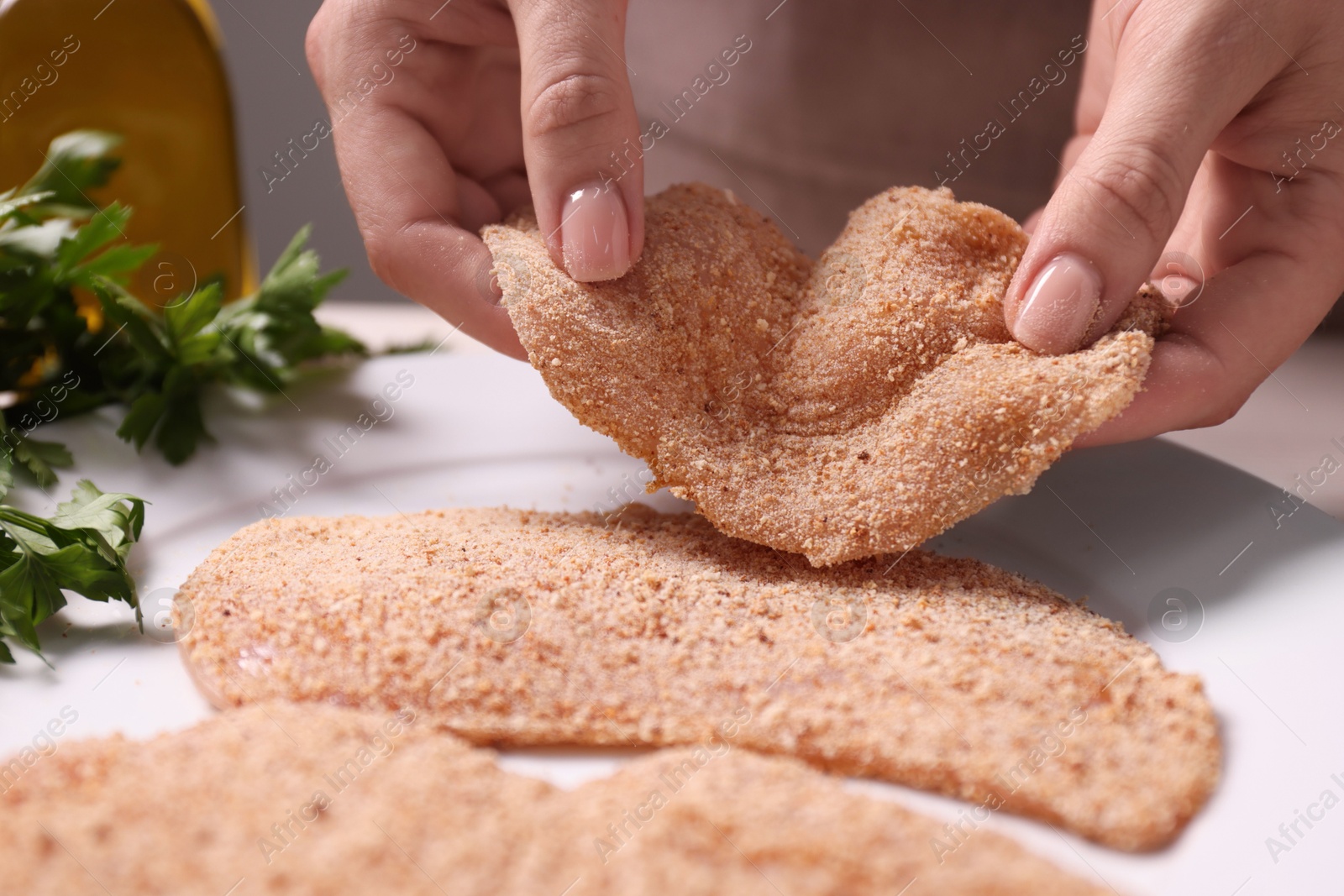 Photo of Making schnitzel. Woman putting slice of meat with bread crumbs onto plate at table, closeup