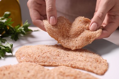 Making schnitzel. Woman putting slice of meat with bread crumbs onto plate at table, closeup