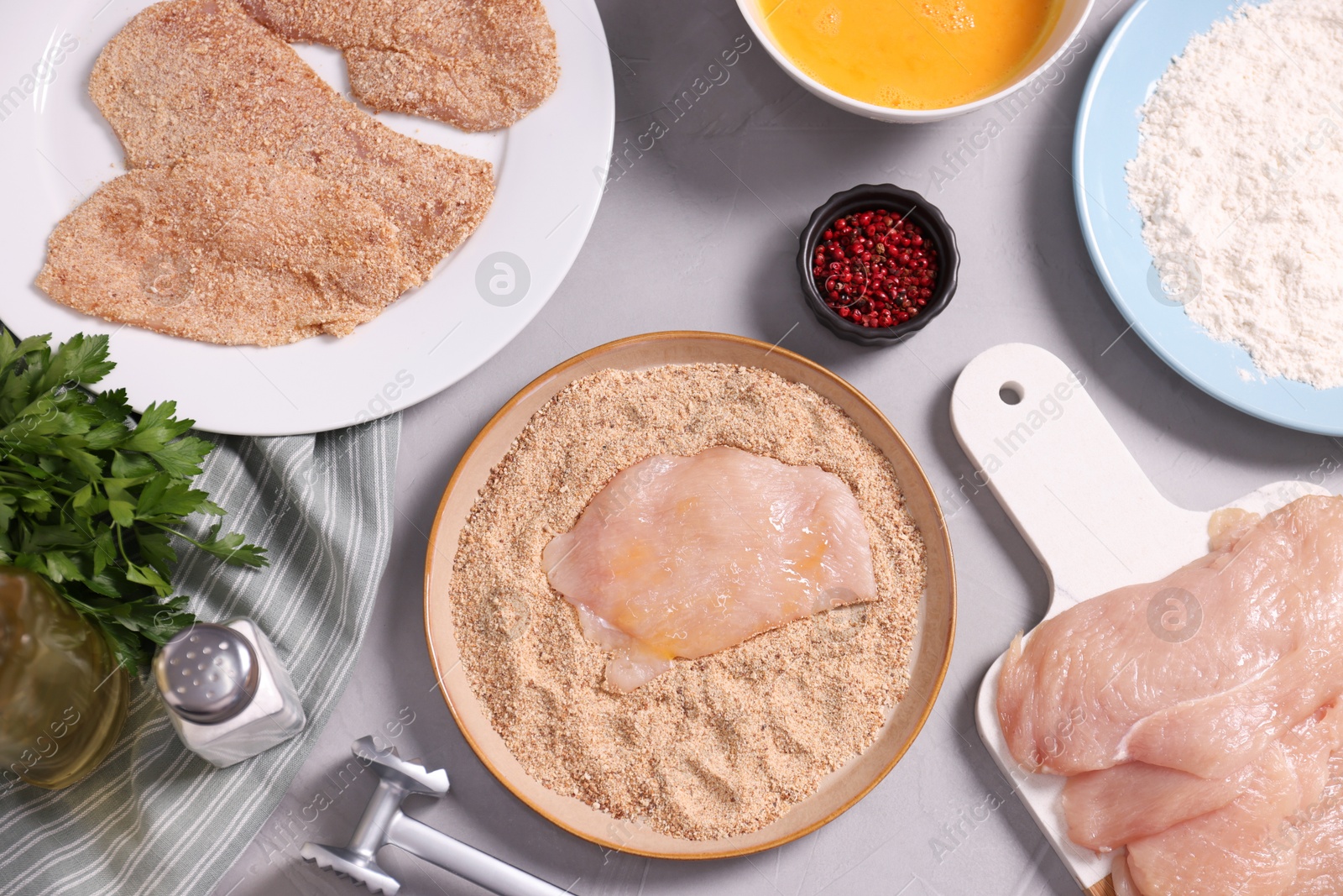 Photo of Making schnitzel. Plate with raw slice of meat in bread crumbs on grey table, flat lay