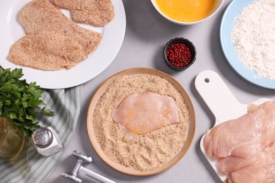 Photo of Making schnitzel. Plate with raw slice of meat in bread crumbs on grey table, flat lay