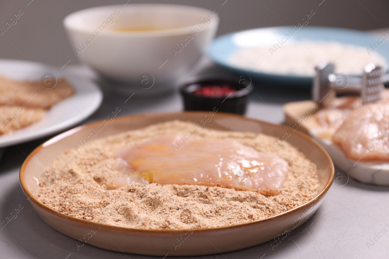 Photo of Making schnitzel. Plate with raw slice of meat in bread crumbs on grey table, closeup