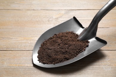 Photo of Metal shovel with soil on wooden table, closeup. Space for text