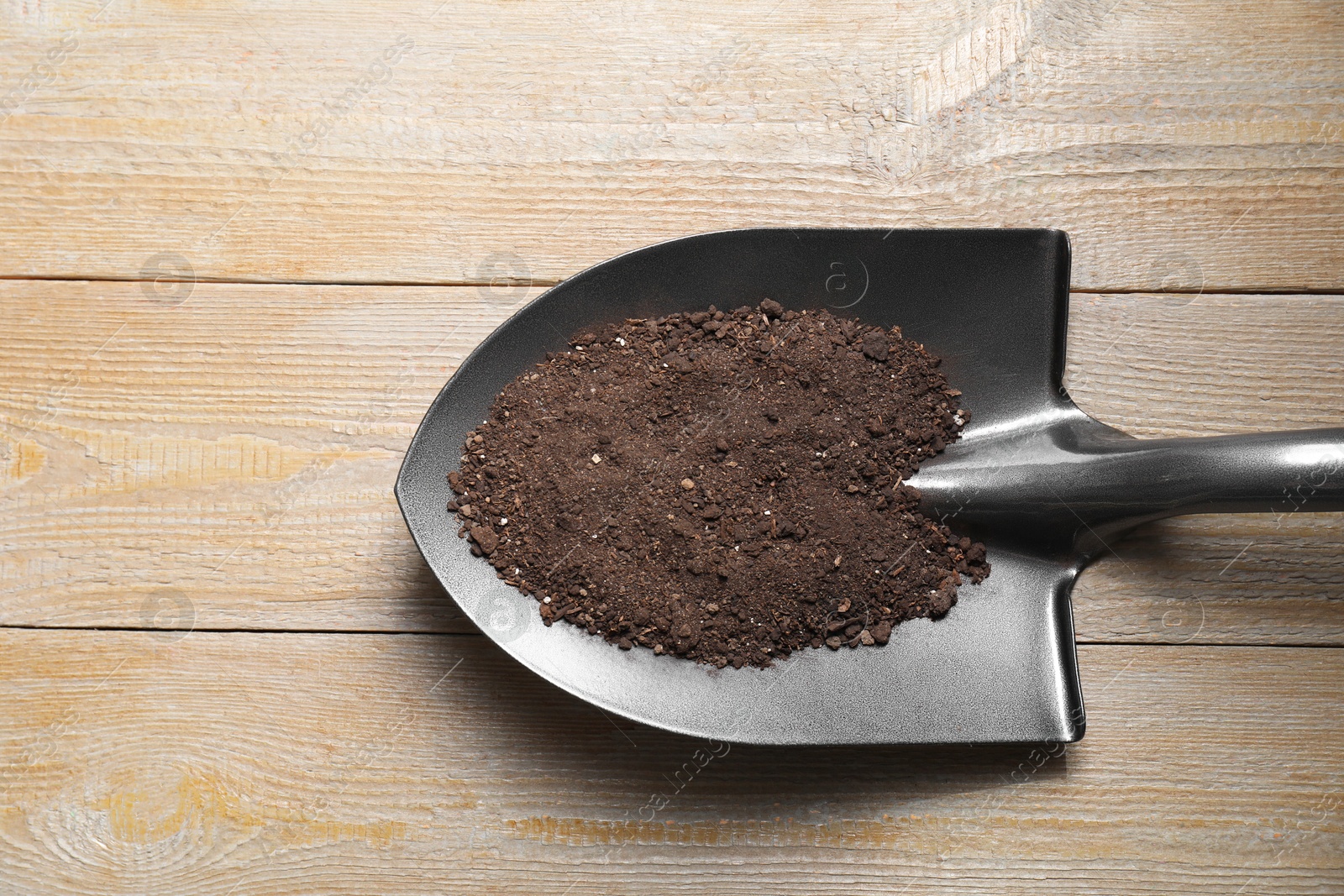 Photo of Metal shovel with soil on wooden table, top view