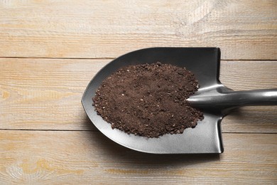 Photo of Metal shovel with soil on wooden table, top view