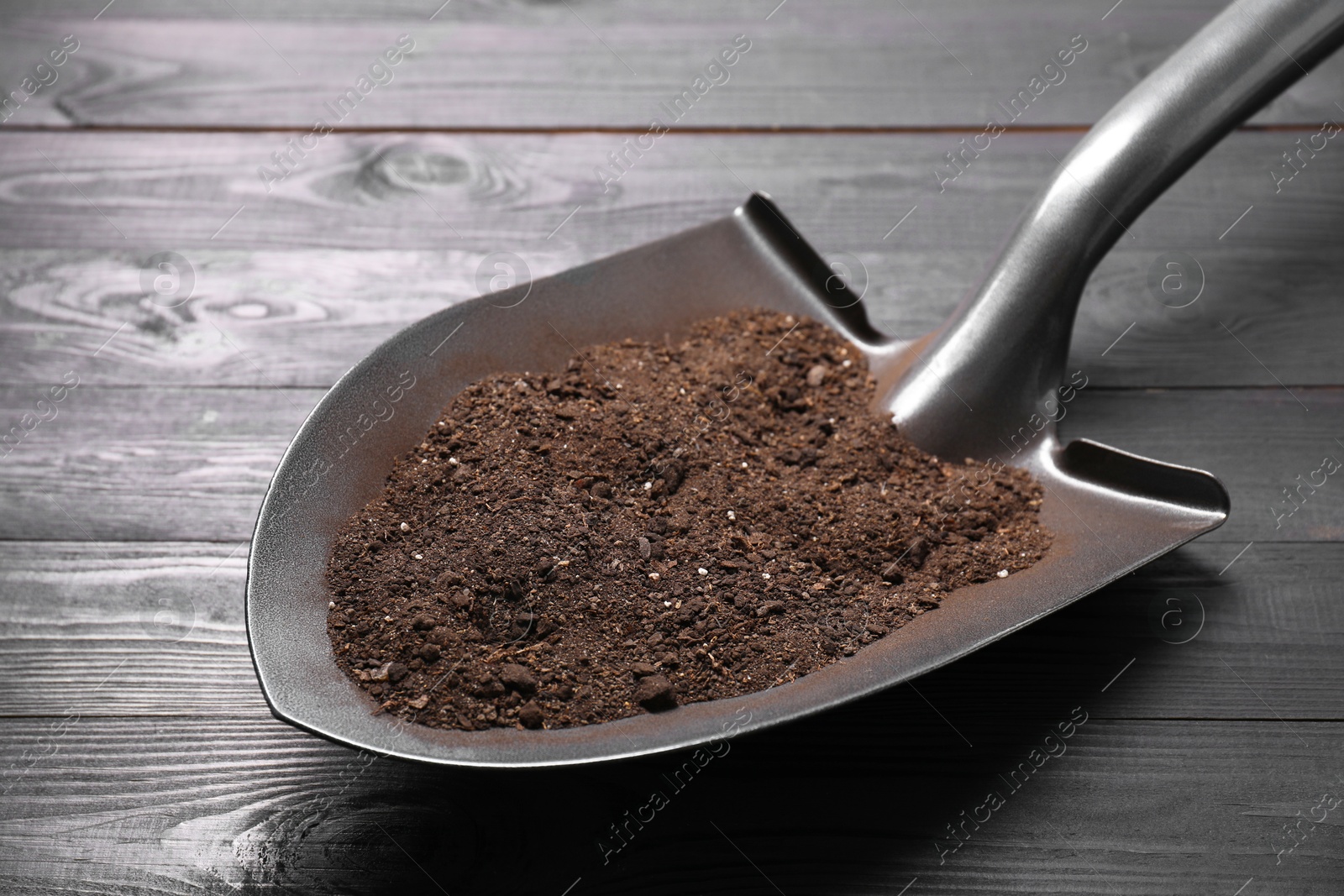 Photo of Metal shovel with soil on black wooden table, closeup