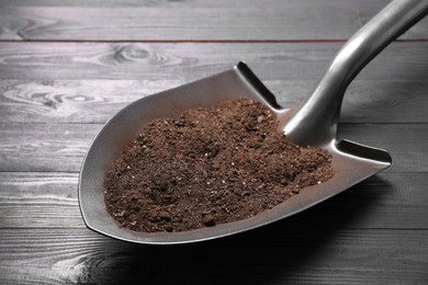 Photo of Metal shovel with soil on black wooden table, closeup