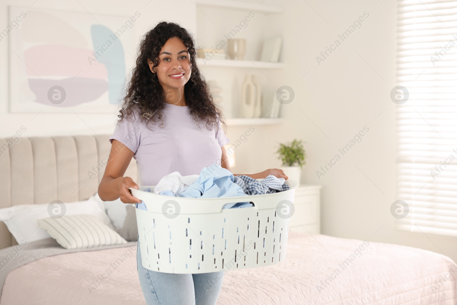 Photo of Happy woman with basket full of laundry in bedroom, space for text