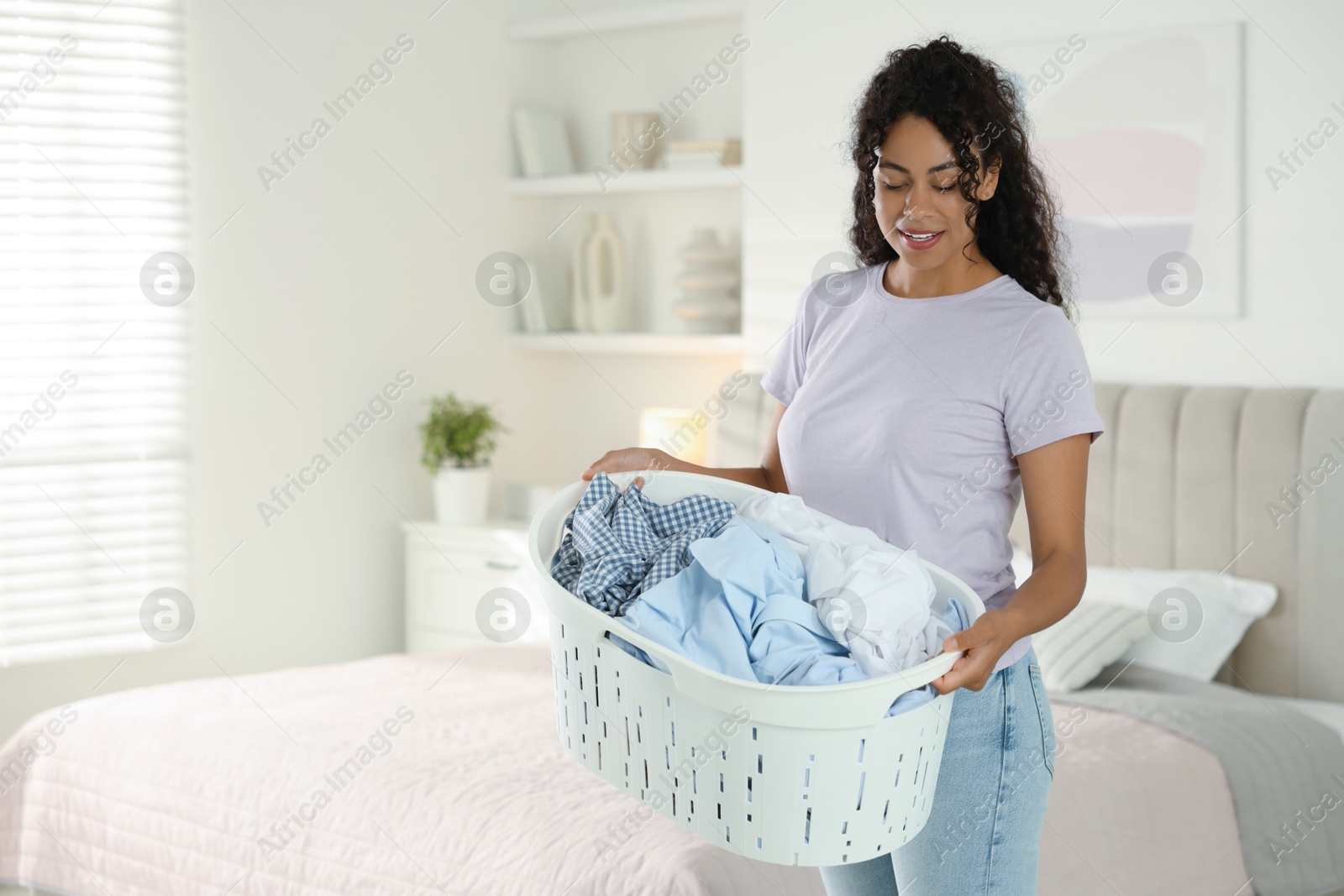 Photo of Happy woman with basket full of laundry in bedroom, space for text