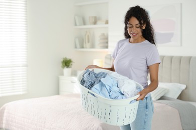 Happy woman with basket full of laundry in bedroom, space for text