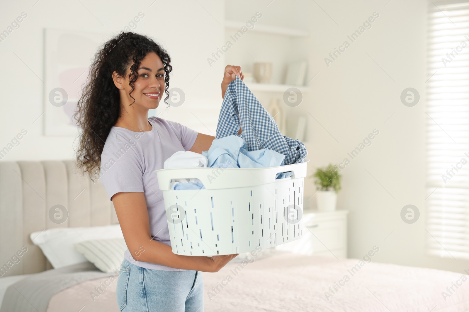 Photo of Happy woman with basket full of laundry in bedroom, space for text