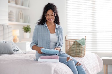 Happy woman with laundry near basket on bed at home