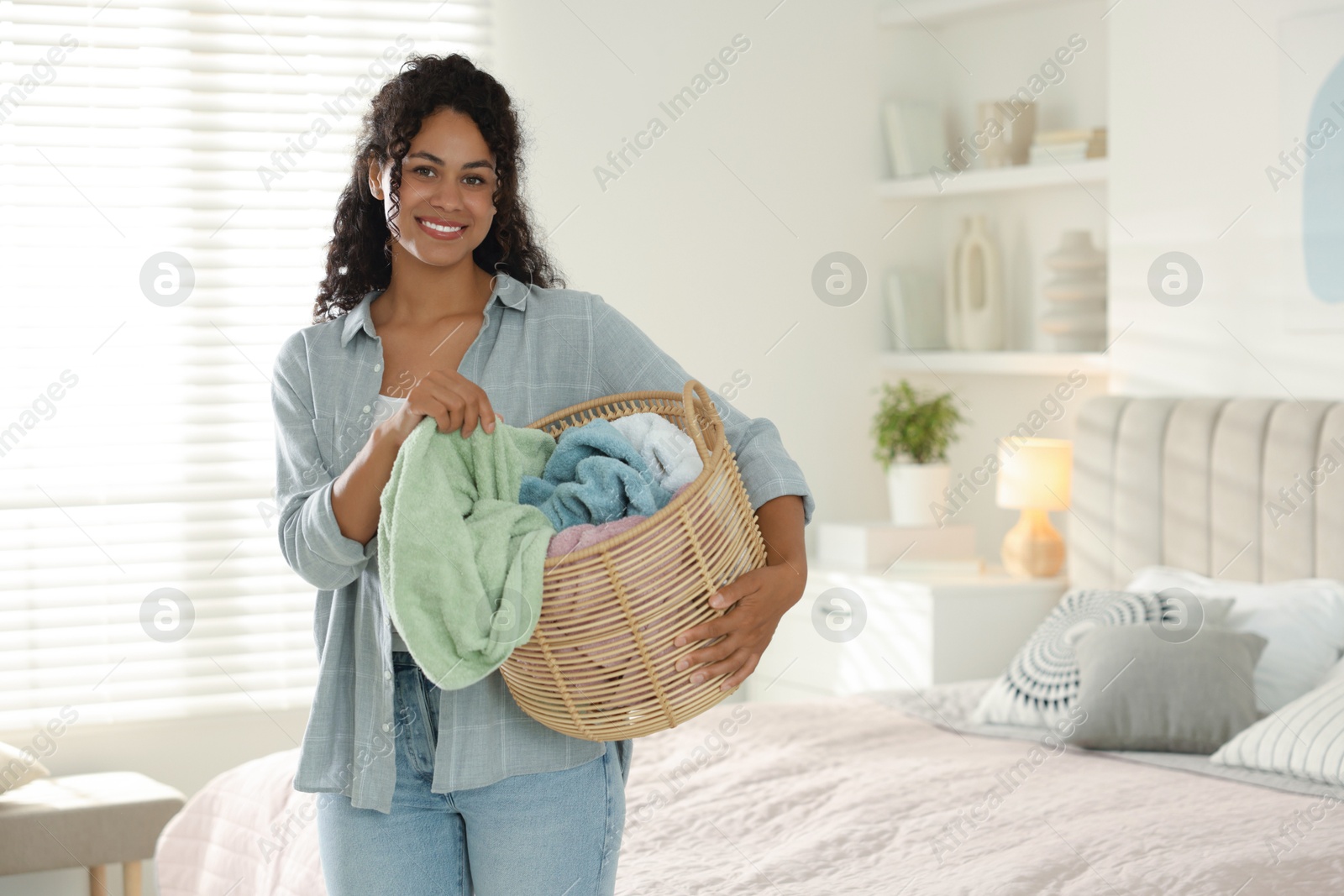 Photo of Happy woman with basket full of laundry in bedroom