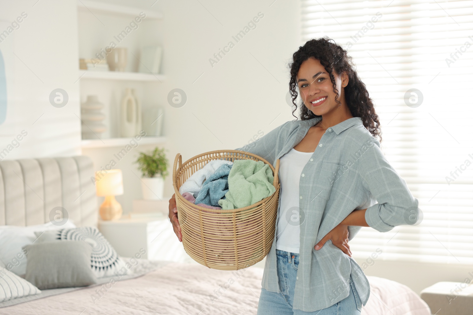 Photo of Happy woman with basket full of laundry in bedroom