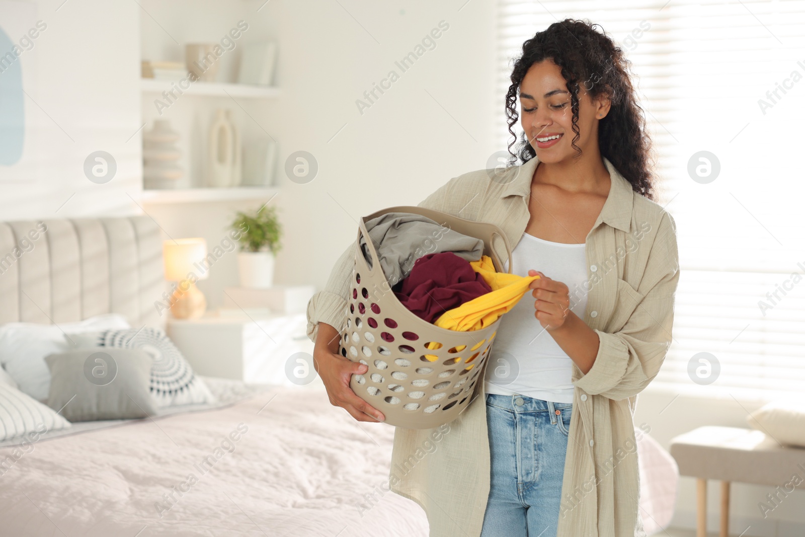 Photo of Happy woman with basket full of laundry in bedroom