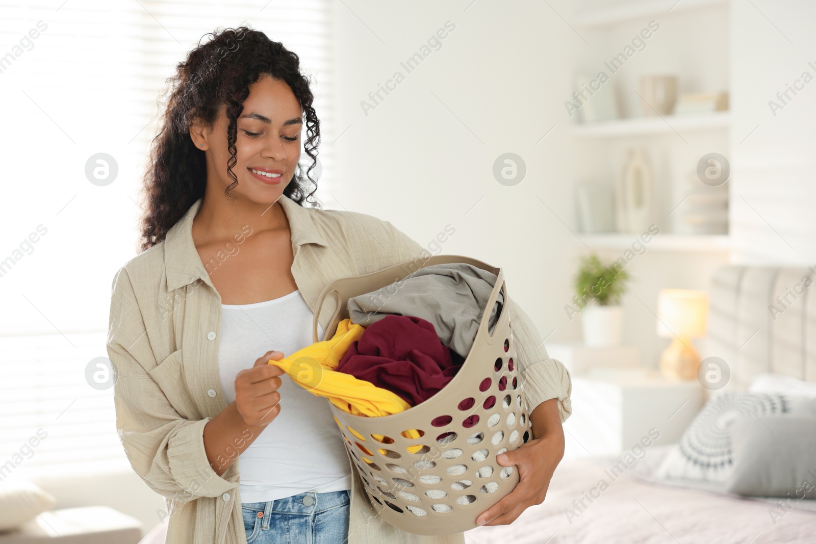 Photo of Happy woman with basket full of laundry in bedroom