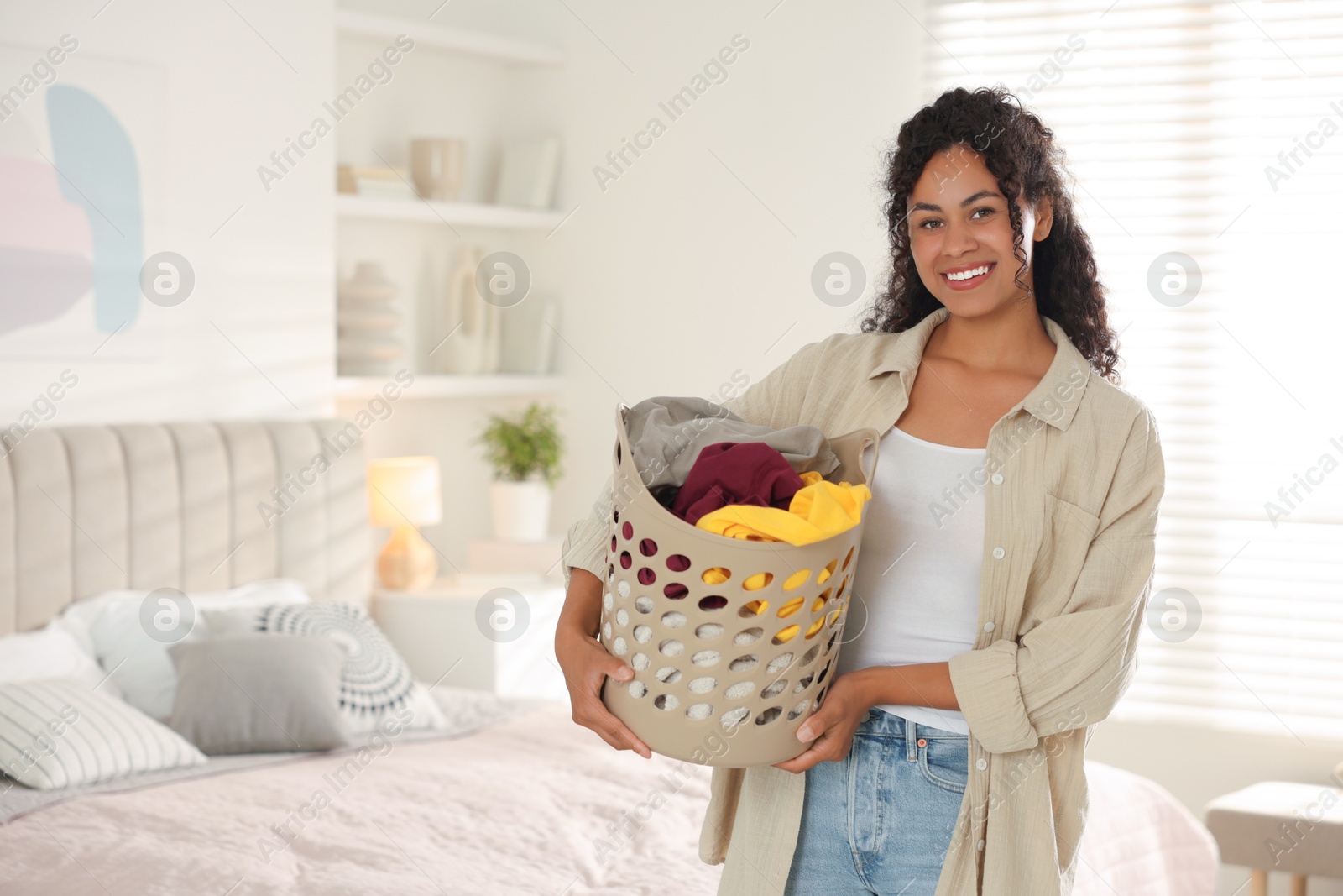 Photo of Happy woman with basket full of laundry in bedroom